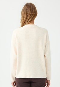 Cremfarbener Pullover mit weicher Textur, entspanntem Schnitt, geripptem Kragen und langen Ärmeln, mit geradem Saum und minimalen Details.