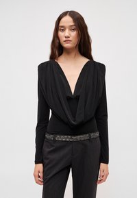 Czarny długi rękaw body z głębokim dekoltem w kształcie litery V i marszczonym materiałem na ramionach, zestawione z dopasowanymi ciemnoszarymi spodniami i zdobionym paskiem.