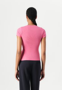 Enges, kurzärmliges rosa T-Shirt aus geripptem Stoff. Rundhalsausschnitt, glatte Textur und kontrastierendes Design zu dunklen Hosen.