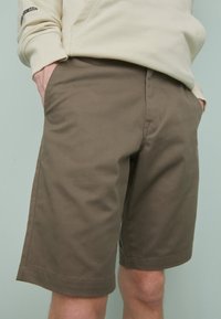 Shorts kaki en tissu mélangé coton résistant, dotés de poches avant, d'une coupe droite et d'une texture lisse avec des coutures soignées.