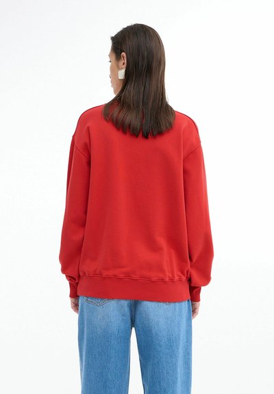 Rød sweatshirt med en afslappet pasform, ribbede manchetter og kant. Glat tekstur, enkelt design, parret med lyseblå vidde bukser.