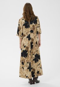 Rochie maxi florală cu model bej și negru, mâneci scurte și detaliu la spate cu decupaj tip cheie. Materialul pare moale, cu o siluetă fluidă.