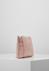 Růžová kabelka z umělé krokodýlí kůže se strukturovaným designem, která má hladký povrch a detail bočního madla.