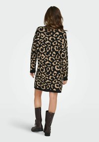 Robe en tricot avec un imprimé léopard noir et beige, manches longues, coupe décontractée, et poignets et ourlet côtelés. Portée avec des bottes marron hautes.