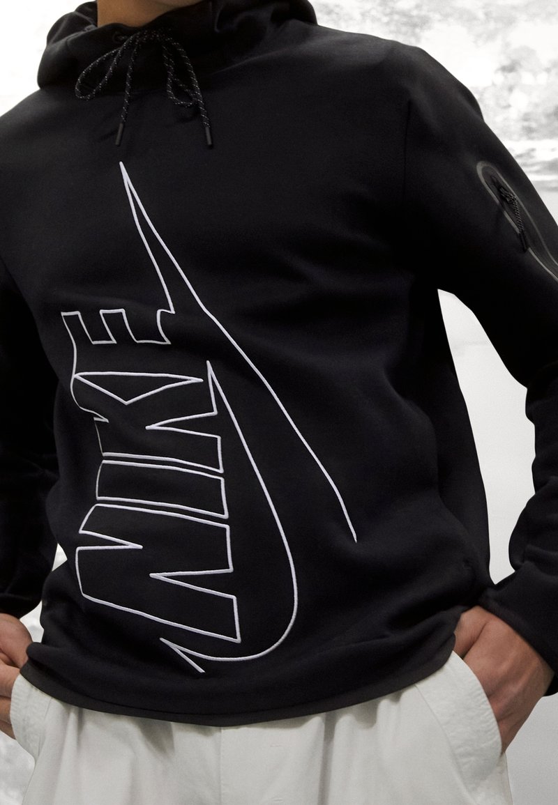 Sudadera negra con capucha que presenta un gran logo de Nike en blanco en la parte frontal, con un tejido texturizado y cordones ajustables en la capucha.
