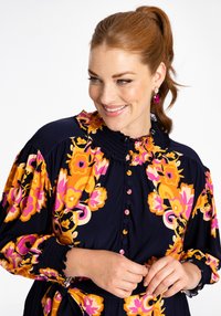 Blumenkleid in Navy mit lebhaften pinken und orangen Mustern. Mit einem gerafften Kragen, durchgehender Knopfleiste und puffigen Ärmeln mit strukturierten Bündchen.