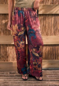 Pantalon d'intérieur ample à fleurs violet avec une surface texturée, présentant des motifs colorés en rouge, or et bleu. Taille élastique.