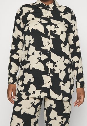 Chemise boutonnée noire et crème avec un motif de feuilles, manches longues et ourlet incurvé. Le tissu présente un aspect texturé.