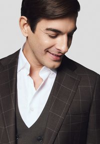 Brązowy garnitur w wzory z białą koszulą pod spodem, prezentujący dopasowany krój i gładką tkaninę, podkreślając podwójnie zapinany kamizelkę.