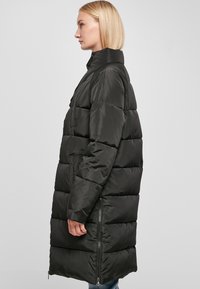 Giubbotto imbottito nero con colletto alto, design trapuntato e dettagli con zip ai lati. Il tessuto ha una consistenza liscia e lucida.
