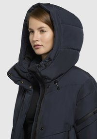 Navy puffer jacket with a large hood, featuring quilted sections, zip closure, snap buttons, and drawcords for adjustable fit.