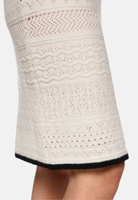 Strickrock in Creme mit strukturierten Mustern, offen gearbeiteten Details und einem schwarzen Saumakzent. Eng anliegendes und knielanges Design.