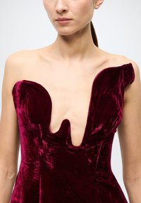 Burgundy velvet dress with a deep V-neckline and structured shoulders. The fabric has a soft, rich texture and slight sheen.