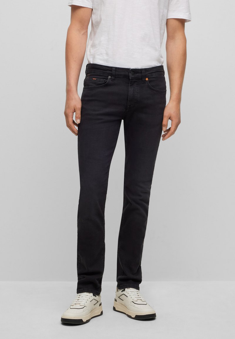 Jeans neri slim-fit realizzati in denim, con cinque tasche, zip frontale e chiusura a bottone, e dettagli di cuciture sottili.