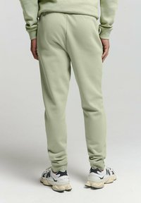 Lichtgroene trainingsbroek met een taps toelopende pasvorm en elastische tailleband, gedragen met wit-zwart sneakers. Zachte textuur, geen zichtbare patronen.