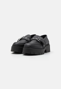 Chaussures à plateforme noires avec une finition en cuir lisse, dotées d'une large sangle en métal argenté et d'un design à bout arrondi.