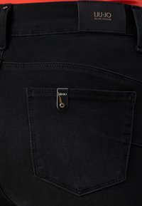 Zwarte denim jeans met een zilveren hardware accent op de achterzak en een label met de tekst "LIU-JO BLUE DENIM."