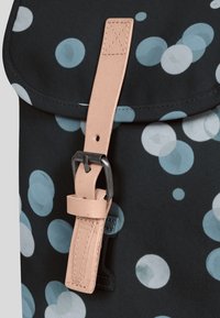 Ryggsäck med svart tyg och blå och ljusblå cirkulära mönster, accentuerad med ett ljusbrunt läderrem och metallspänne.