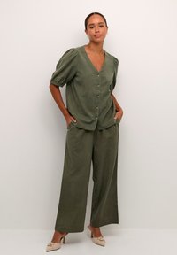 Ensemble en lin vert olive composé d'un haut boutonné avec des manches bouffantes et un pantalon à jambes larges. Texture lisse avec un minimum de détails.