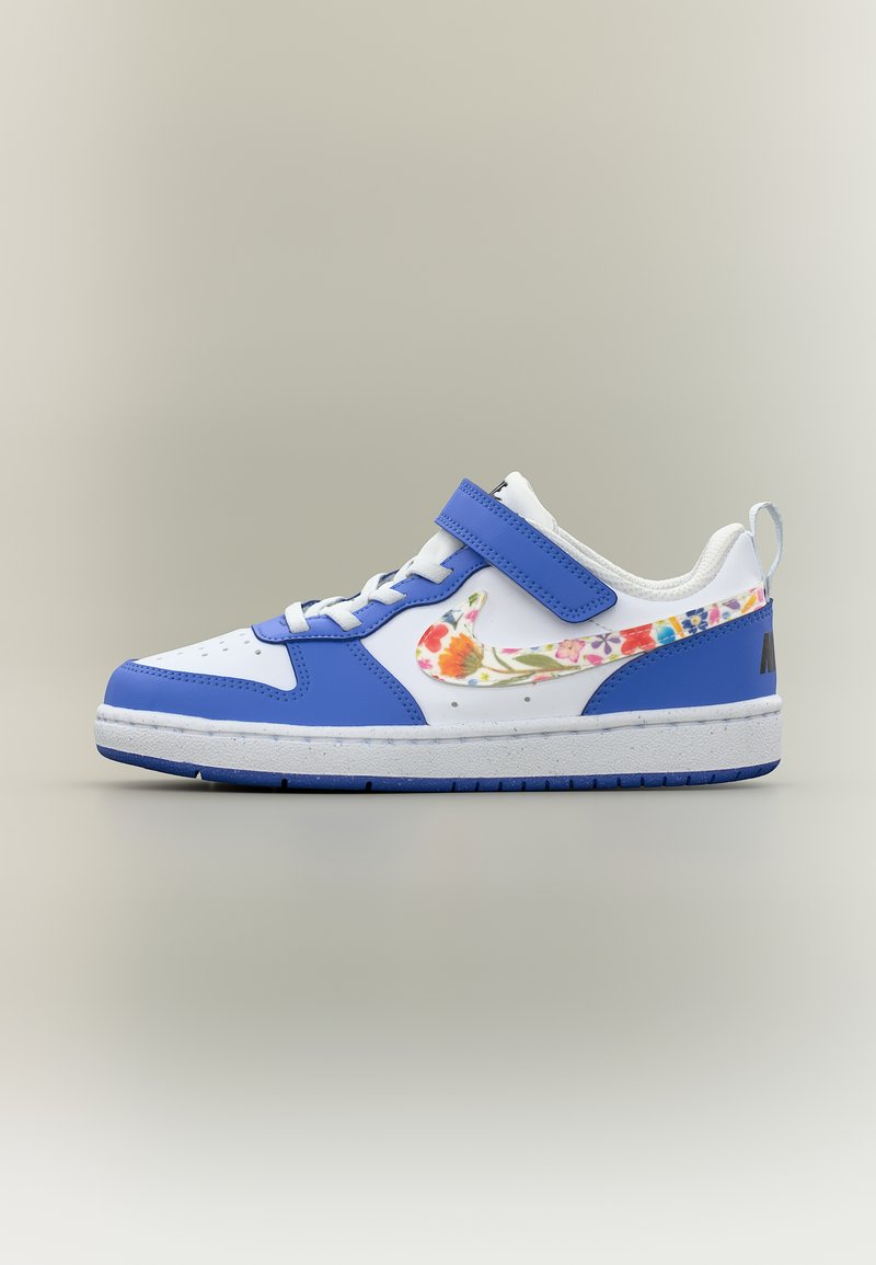 Άσπρο και μπλε αθλητικό παπούτσι με λουλουδάτο λογότυπο Nike, λουράκι με βέλκρο, κορδόνια και χοντρή σόλα σε ουδέτερο φόντο.