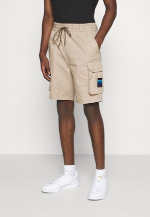 Beige cargo shorts med elastisk talje, justerbar snor, sidelomme og et farverigt mærke med bjerge.