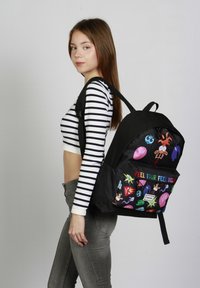 Mochila negra con estampados de personajes de dibujos animados coloridos, cuenta con un bolsillo frontal que dice "Siente tus sentimientos", correas ajustables y tejido resistente.