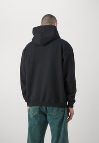 Czarna bluza z dużym, usztywnianym kapturem, ściągaczami na rękawach i dolnym brzegu, zestawiona z turkusowymi dżinsami o luźnym kroju i casualowym designie.