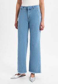 Jean large bleu clair avec un ourlet effiloché, en denim, doté d'une taille haute et de poches avant. Associé à des chaussures argentées à bout pointu.