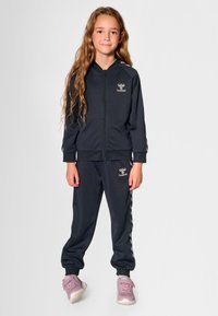 Ciemnoszary sportowy dres wykonany z gładkiej tkaniny, składający się z bluzy na zamek z logo oraz dopasowanych spodni z bocznymi paskami.