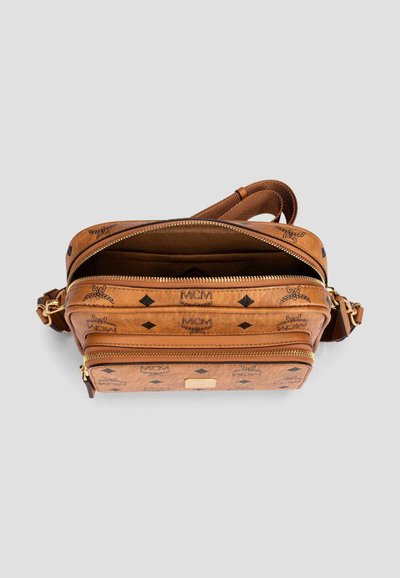 Brown MCM crossbody bag with two zippered compartments, adjustable strap, and logo pattern on a plain light background.