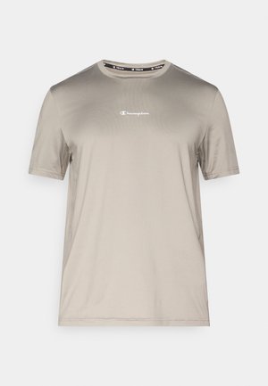 Gaiši bēša īsroku krekls no gluda auduma ar apaļu kakla izgriezumu un nelielu baltu Champion logotipu uz krūtīm.