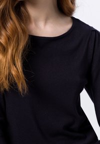 Zwarte gebreide top met een ronde halslijn, lange mouwen en een soepele textuur; de stof heeft een lichte rek en subtiele tonale variaties.