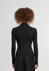 Čierny dlhý rukáv s vysokým golierom, vyrobený z hladkej látky. Priliehavý strih zužujúci sa v oblasti pásu, s minimálnymi švami.