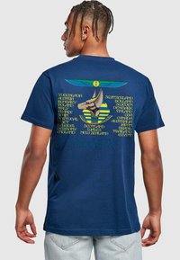 Marineblaue Baumwoll-T-Shirt mit einem grafischen Design eines Hundes im ägyptischen Thema und Text, der verschiedene Länder sowie "Welt-Sklaverei-Tour 1984-85" auflistet.