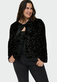 Črna bleščeča jakna z satensko kravato spredaj; ima mehak teksturo in skrajšano obliko z dolgimi rokavi in zaobljenim izrezom.