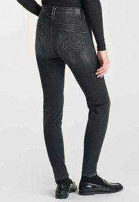 Jeans en denim noir taille haute avec une coupe slim, présentant une couture décorative sur les poches arrière et une texture lisse.