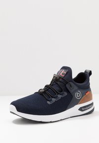 Navy mesh athletic shoe with black laces, brown accent, white sole, logo on side, textured fabric upper, and padded collar for comfort.