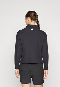 Black long-sleeve polo-style top with a collar and three white stripes logo at the back, paired with black shorts. Smooth fabric texture.