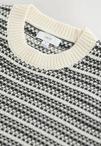 Maglione a maglia con colletto a coste crema, motivo geometrico in bianco e nero e un'etichetta che recita "NEXT" con taglia "M."
