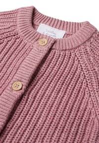 Cardigan tricoté en rose doux, présentant une texture côtelée, un col rond et deux boutons clairs sur la patte de boutonnage. Étiquette visible à l'intérieur.