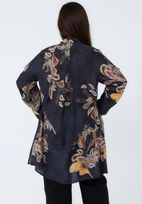 Black, long-sleeve blouse with a paisley pattern in gold, orange, and cream. Lightweight fabric with a loose fit and side slits.