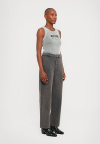 Sivi rebrasti top bez rukava s natpisom "Moschino Jeans", uparen s sivo visokim farmerkama širokih nogavica i crnim čizmama na petu sa srebrnim detaljima.