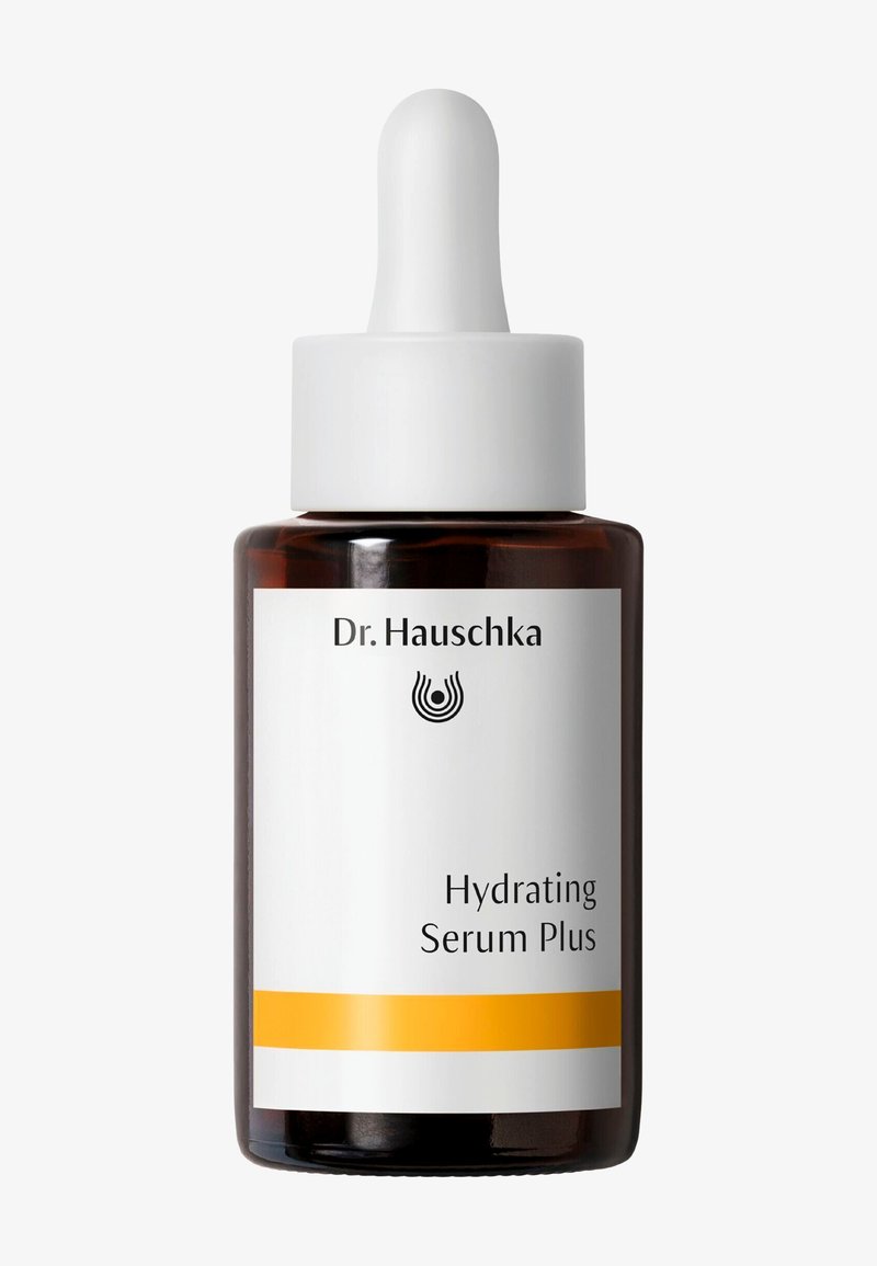 Flacon compte-gouttes en verre brun étiqueté Dr. Hauschka Hydrating Serum Plus avec bouchon blanc et bande jaune sur l’étiquette sur fond blanc.