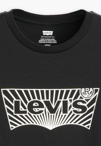 T-shirt en coton noir avec un logo Levi's blanc bien visible et un design de lignes radiales sous l'encolure. Étiquette visible à l'intérieur du col.