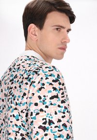 Giacca grafica con un patrones astratto colorato in rosa, nero, teal e pesca. Tessuto morbido, collo bianco e design rilassato.