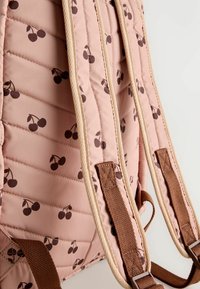 Pink padded backpack with brown cherry prints and beige-edge padded shoulder straps against a neutral background.