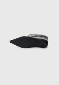 Black pointed-toe boot lying on its side showing the smooth sole and slightly slouched upper against a plain background.