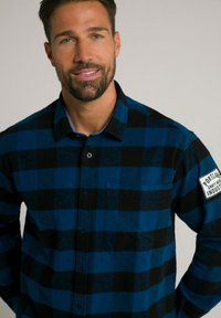 Blauw en zwart geruite flanellen shirt met knoopsluiting aan de voorkant, een enkele borstzak en een logo patch op de mouw. Zachte textuur.