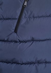 Primo piano di giacca imbottita blu navy che mostra cuciture orizzontali e una cerniera verticale nera.