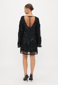 Melna kleita ar caurspīdīgu audumu, garām piedurknēm un ziedu izšuvumu. Atvērts aizmugurējais griezums ar sasaistes detaļu, līdz ceļgaliem, kombinēta ar melnām ikdienas kurpēm.